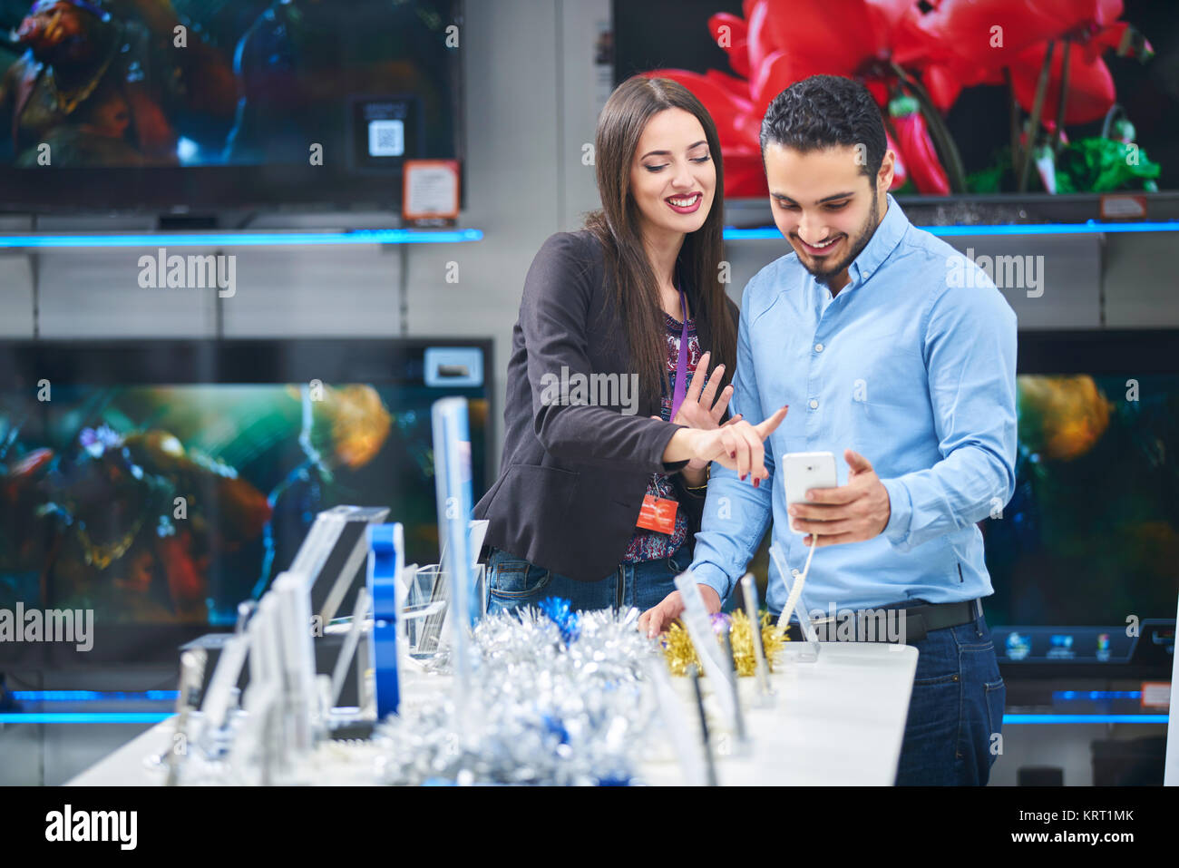 Young couple in consumer electronics store looking at latest laptop, television and photo camera to buy Stock Photo