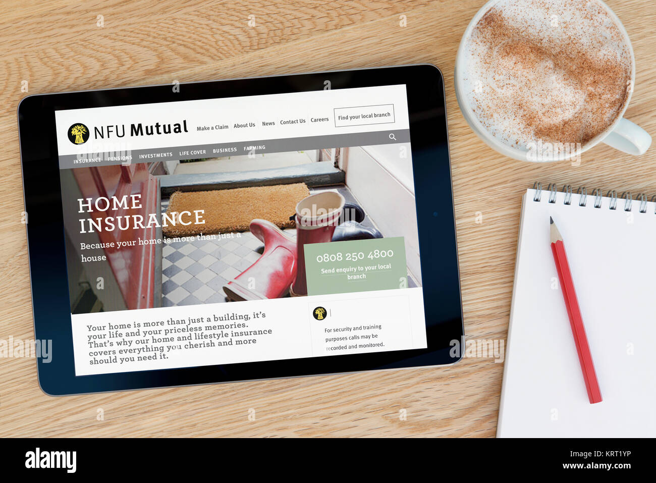 The NFU Mutual website on an iPad tablet device which rests on a wooden table beside a notepad and pencil and a cup of coffee (Editorial only) Stock Photo