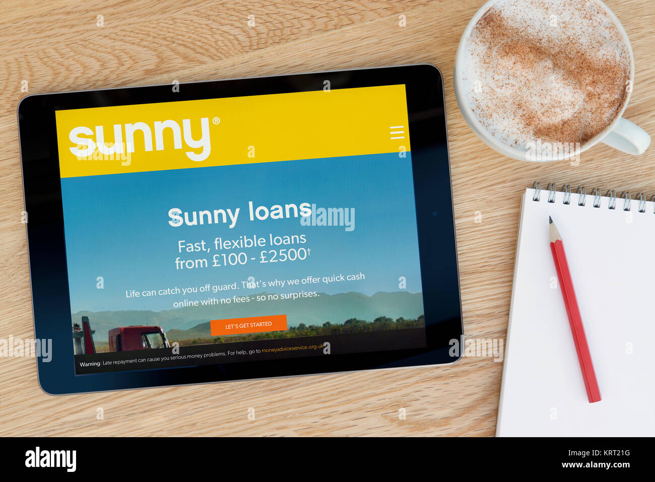 The Sunny website on an iPad tablet device which rests on a wooden table beside a notepad and pencil and a cup of coffee (Editorial only) Stock Photo
