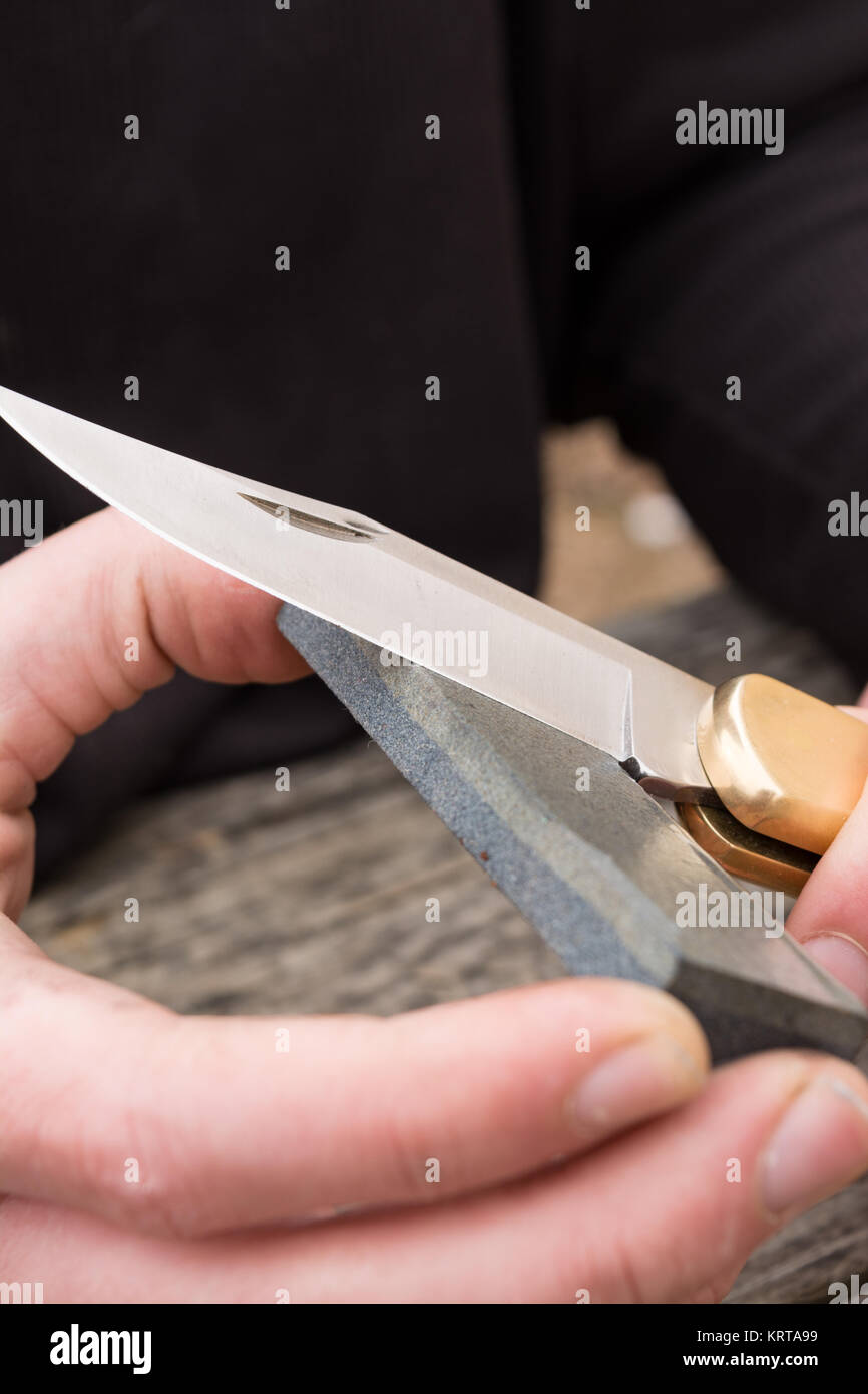 Male hands sharpening large pocket knife with a wetstone. Stock Photo