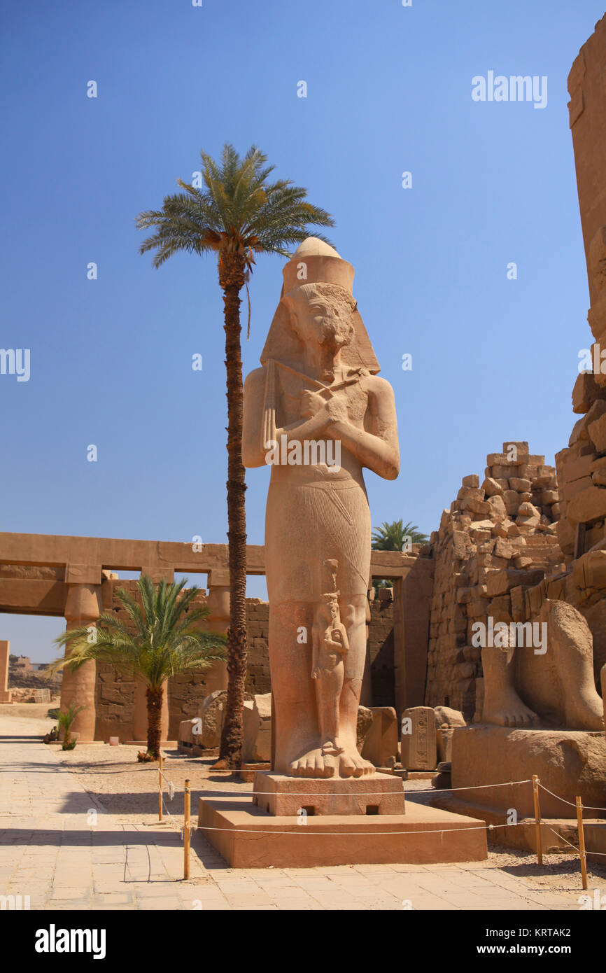 The statue of Ramesses II with crossed arms, holding crook and flail (symbols of kingship), with the small statue of Princess Bent-anta at his fit, Gr Stock Photo