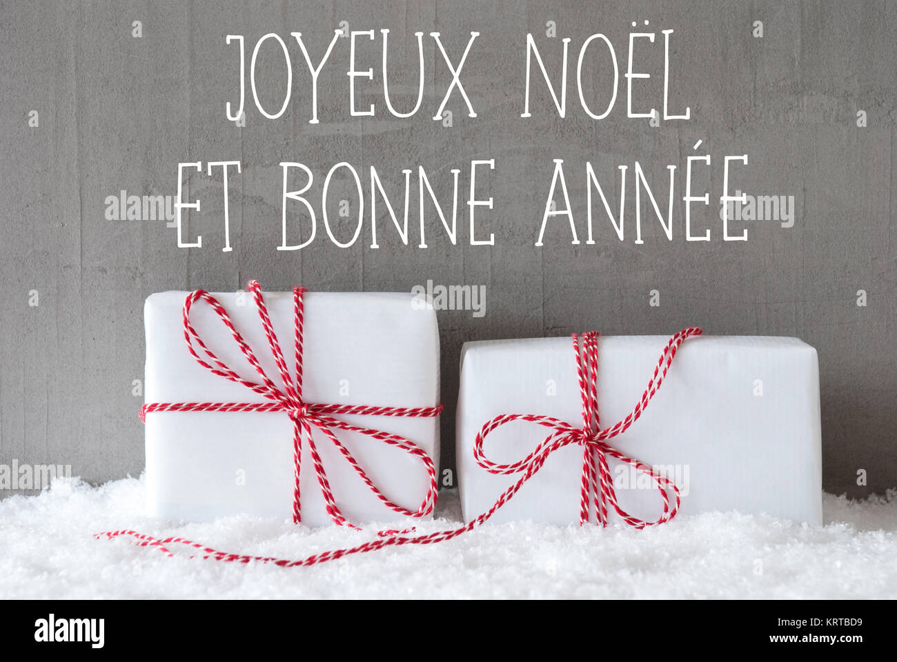 French Text Joyeux Noel Et Bonne Annee Means Merry Christmas And Happy New Year Two White Christmas Gifts Or Presents On Snow Cement Wall As Background Modern And Urban Style Stock Photo