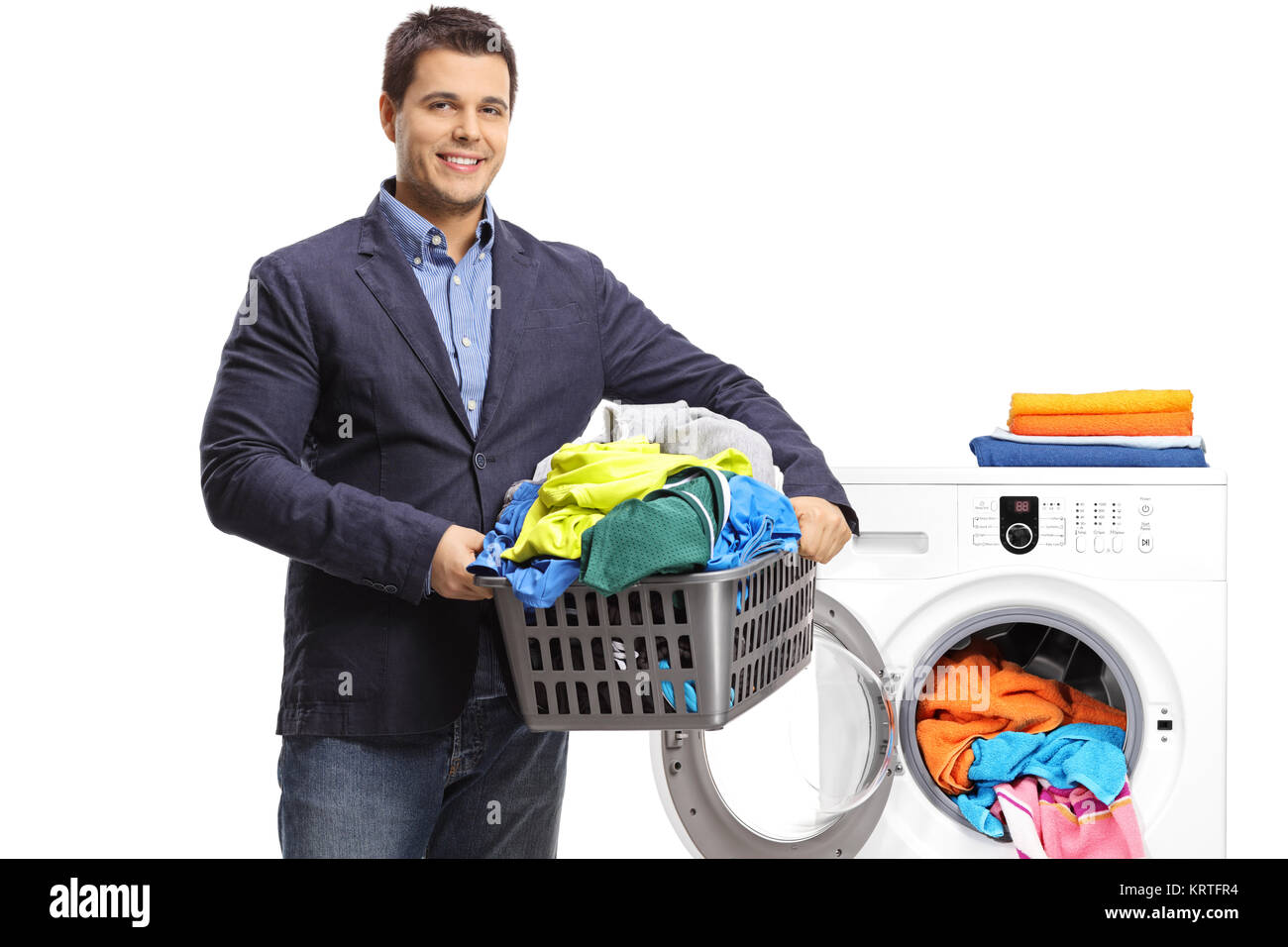 Elegant guy holding a laundry basket filled with clothes in front of a washing machine isolated on white background Stock Photo