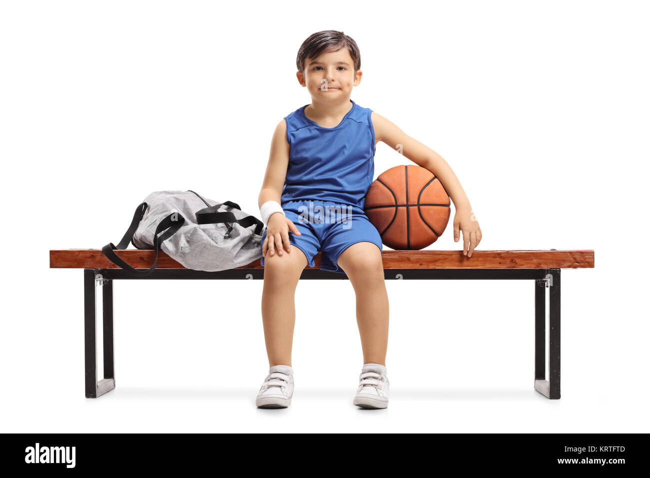 Little basketball player sitting on a wooden bench next to a sports bag