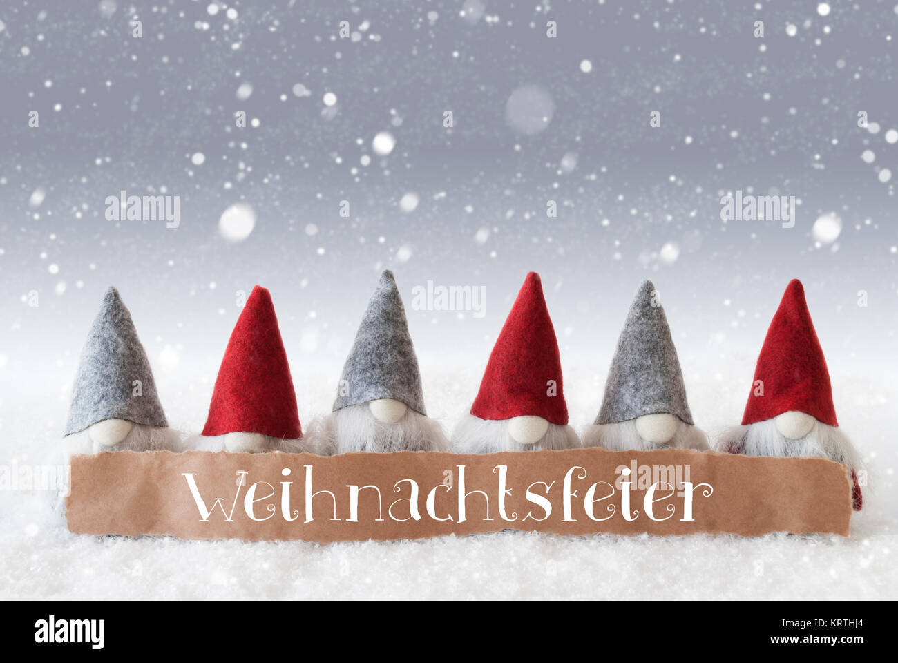 Label With German Text Weihnachtsfeier Means Christmas Party. Christmas Greeting Card With Gnomes. Silver Background With Snow And Snowflakes Stock Photo