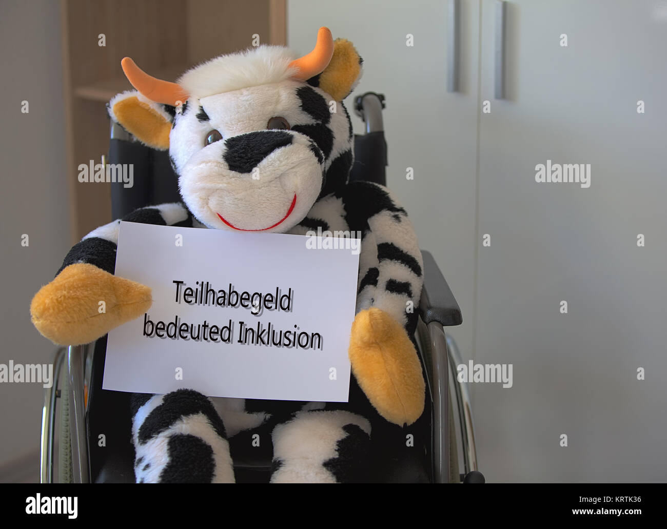 plush cow sitting in a wheelchair and holding a sign Stock Photo