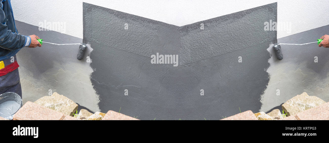 Nahaufnahme Arm eines Anstreicher mit Farbrolle in der Hand streicht eine Hauswand mit grauer Farbe. Stock Photo