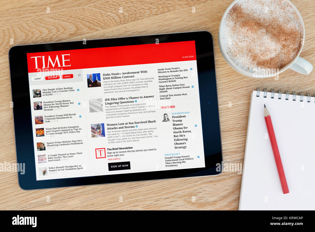 The Time magazine website on an iPad tablet device which rests on a wooden table beside a notepad and pencil and a cup of coffee (Editorial only) Stock Photo
