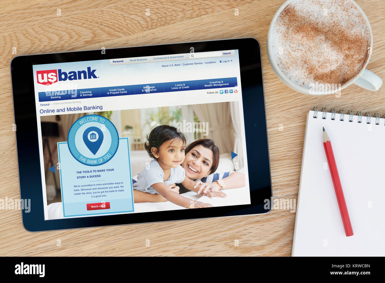 The US Bank website on an iPad tablet device which rests on a wooden table beside a notepad and pencil and a cup of coffee (Editorial only) Stock Photo