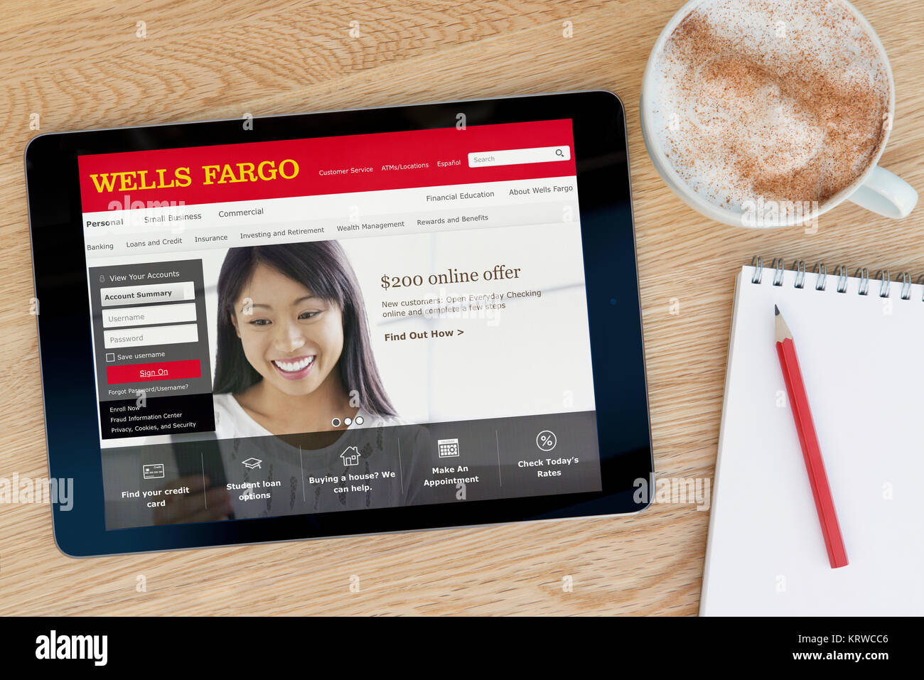 The Wells Fargo website on an iPad tablet device which rests on a wooden table beside a notepad and pencil and a cup of coffee (Editorial only) Stock Photo
