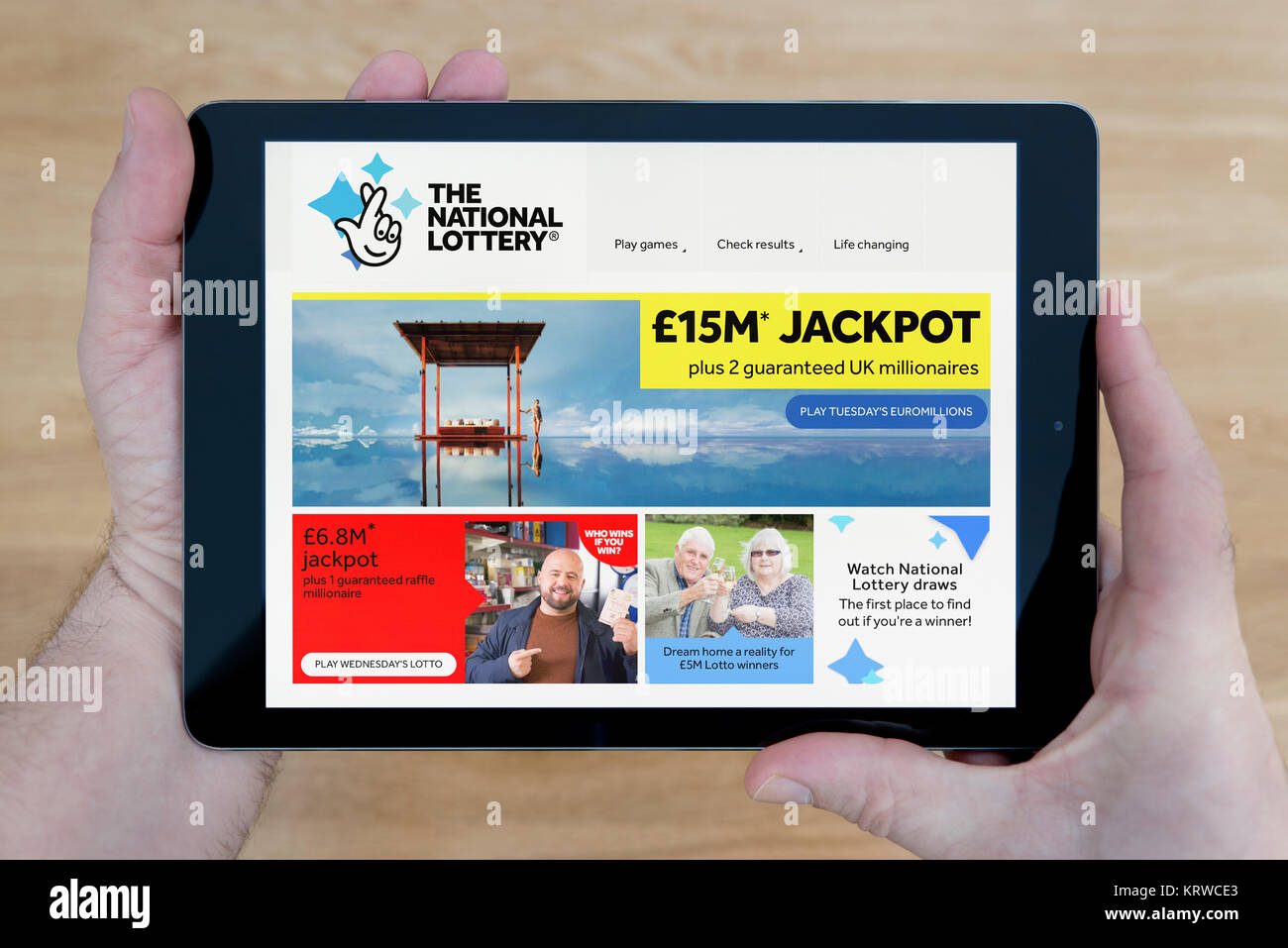 A man looks at the National Lottery website on his iPad tablet device, shot against a wooden table top background (Editorial use only) Stock Photo