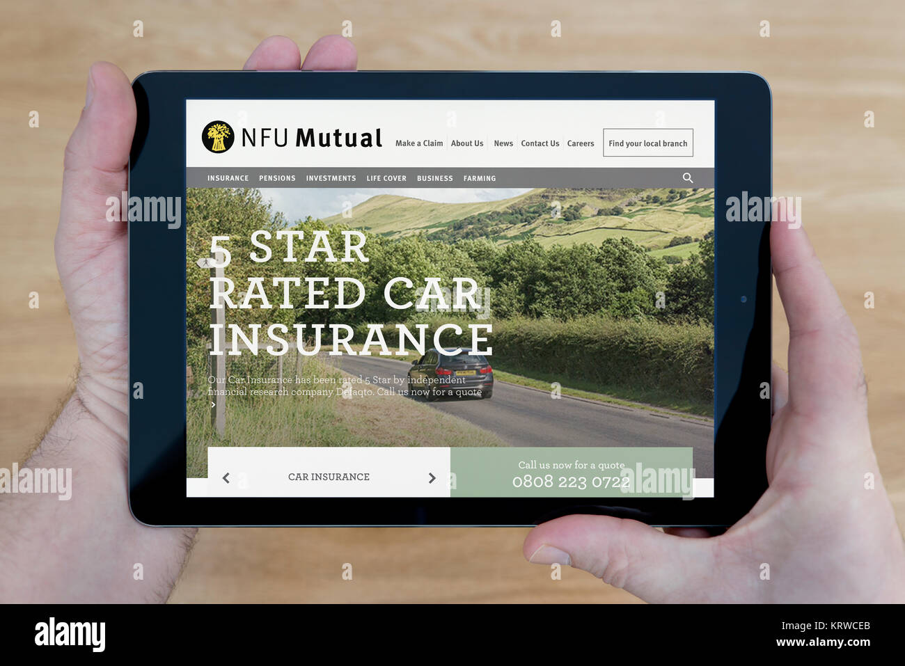 A man looks at the NFU Mutual website on his iPad tablet device, shot against a wooden table top background (Editorial use only) Stock Photo