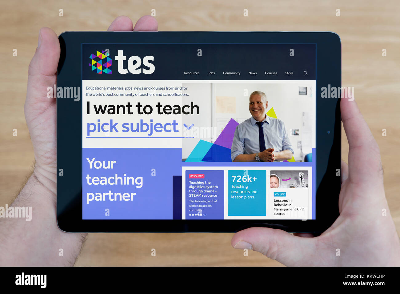 A man looks at the Times Educational Supplement (TES) website on his iPad tablet, shot against a wooden table top background (Editorial use only) Stock Photo