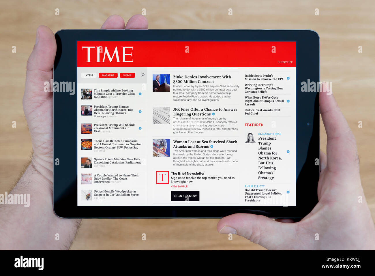 A man looks at the Time Magazine website on his iPad tablet device, shot against a wooden table top background (Editorial use only) Stock Photo