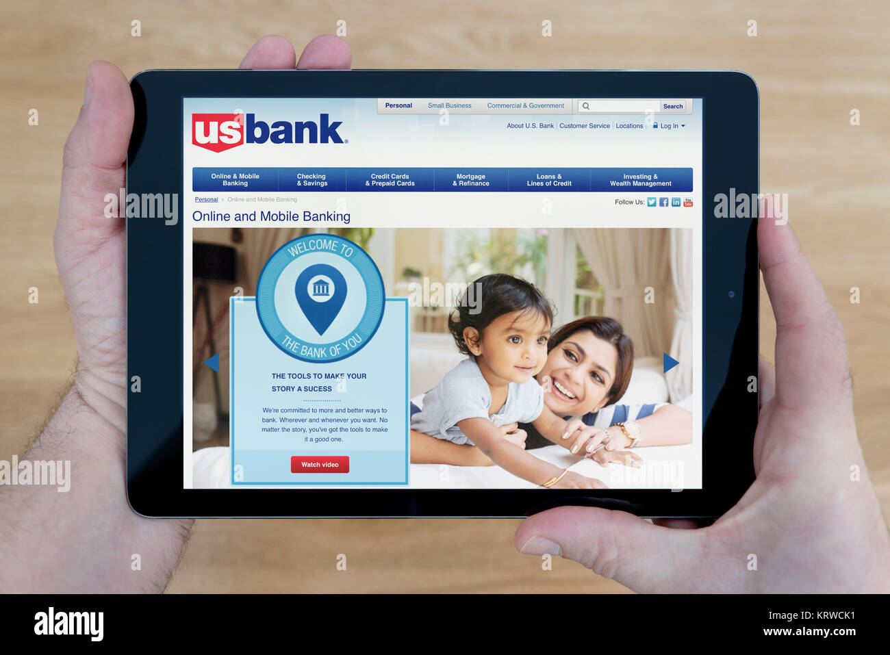 A man looks at the US Bank website on his iPad tablet device, shot against a wooden table top background (Editorial use only) Stock Photo