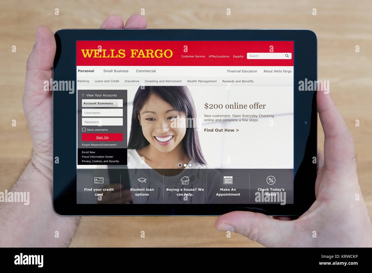A man looks at the Wells Fargo bank website on his iPad tablet device, shot against a wooden table top background (Editorial use only) Stock Photo
