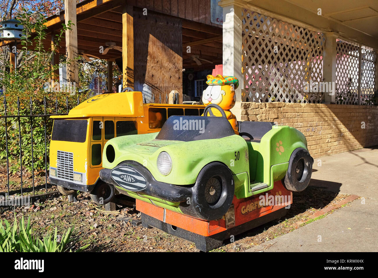 Old discarded children's amusement rides, Garfield Car, and a yellow fire truck, sit abandoned behind closed businesses in a rural Georgia town, USA. Stock Photo