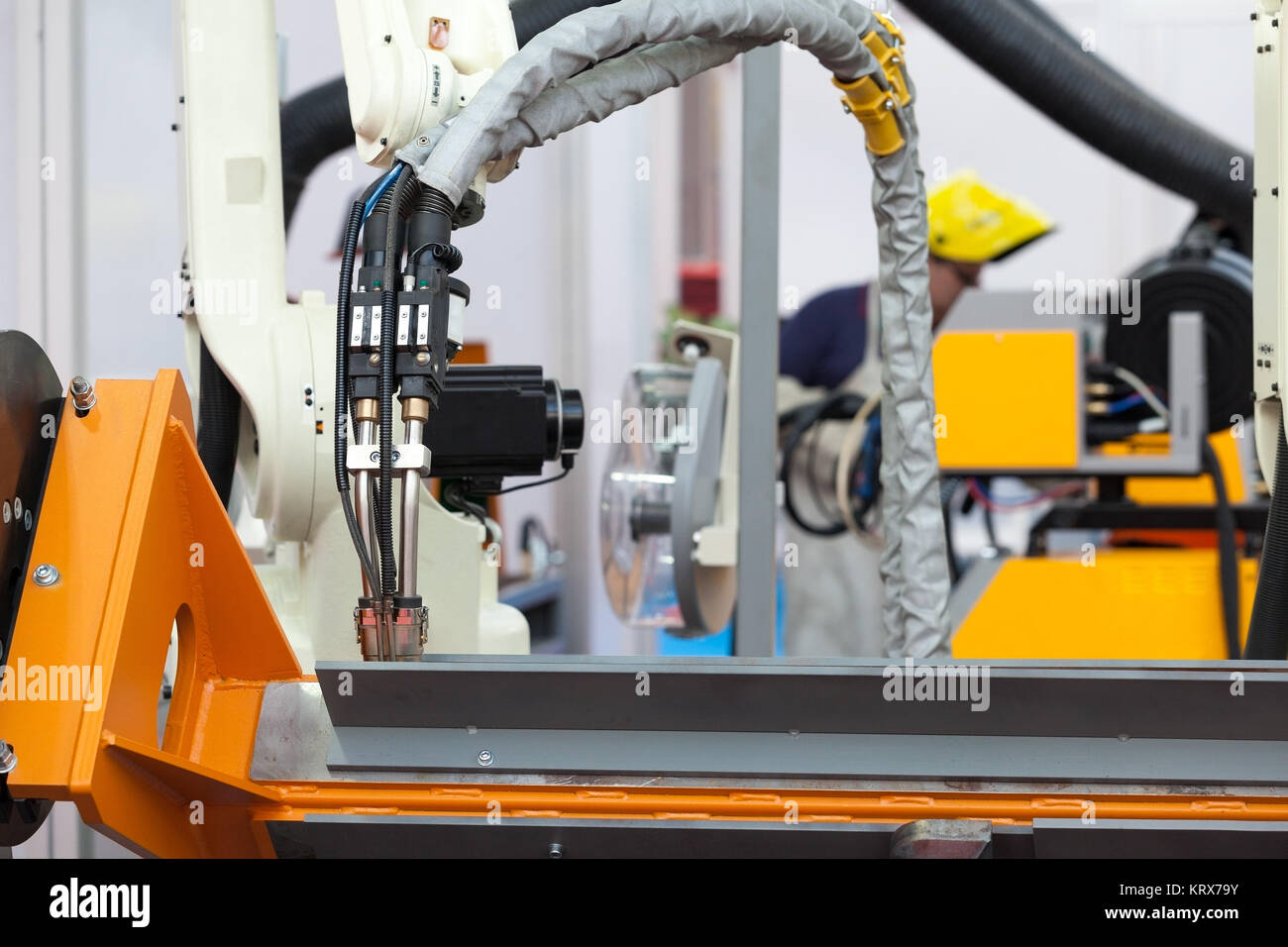 Industrial welding robot arm in the focus, blurred welder in the background Stock Photo