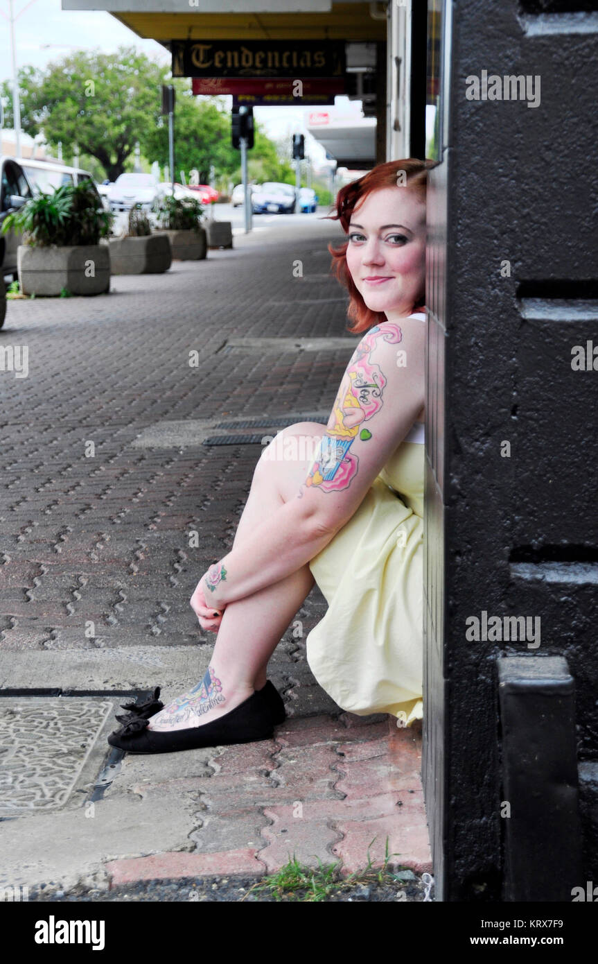 RED HEADED YOUNG WOMEN SITTING ON PAVEMENT STEPS Stock Photo