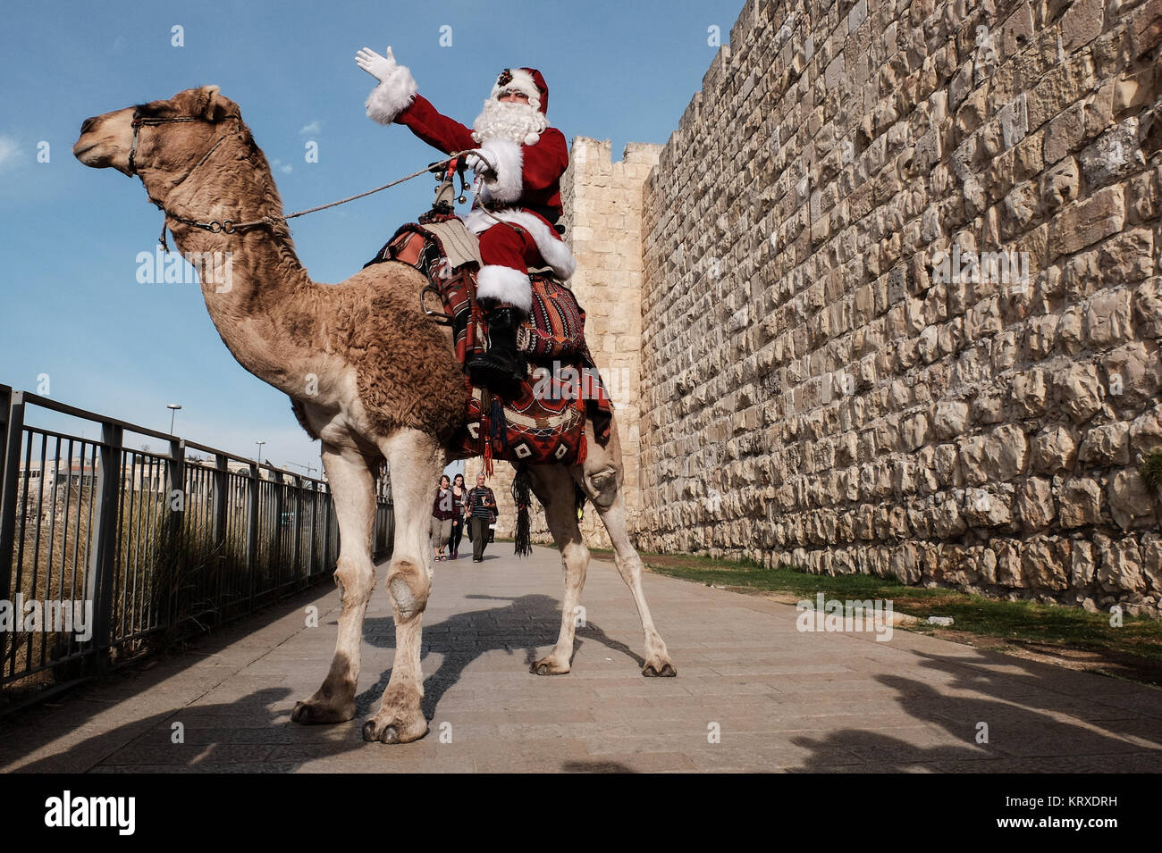 Jerusalem, Israel. 21st December, 2017. Santa Claus, or 'Baba Noel' as he is called in Arabic, rides a camel substitute for rain deer near Jerusalem's Old City Jaffa Gate. The Jerusalem Municipality and the Jewish National Fund distributed specially grown Arizona Cypress Christmas trees to the Christian population at the Jaffa Gate. Credit: Nir Alon/Alamy Live News Stock Photo