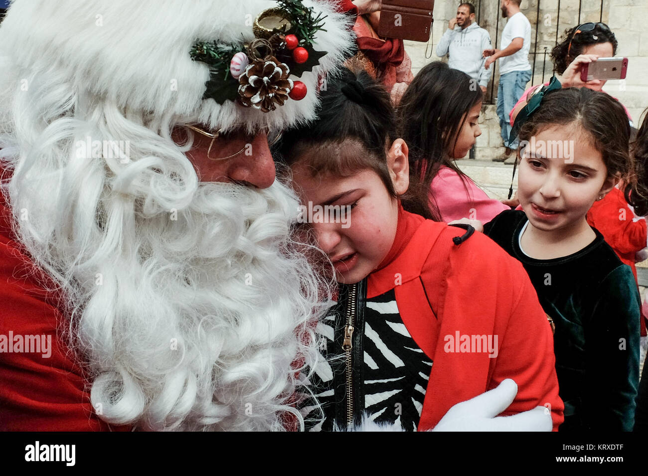 Jerusalem, Israel. 21st December, 2017. Santa Claus, or 'Baba Noel' as he is called in Arabic, comforts a crying young girl near Jerusalem's Old City Jaffa Gate. The Jerusalem Municipality and the Jewish National Fund distributed specially grown Arizona Cypress Christmas trees to the Christian population at the Jaffa Gate. Credit: Nir Alon/Alamy Live News Stock Photo