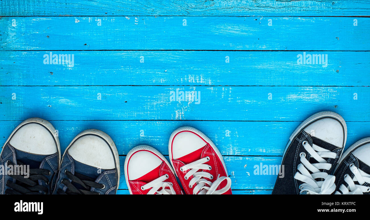 Three pairs of wearing sneakers on a blue wooden surface, top view ...