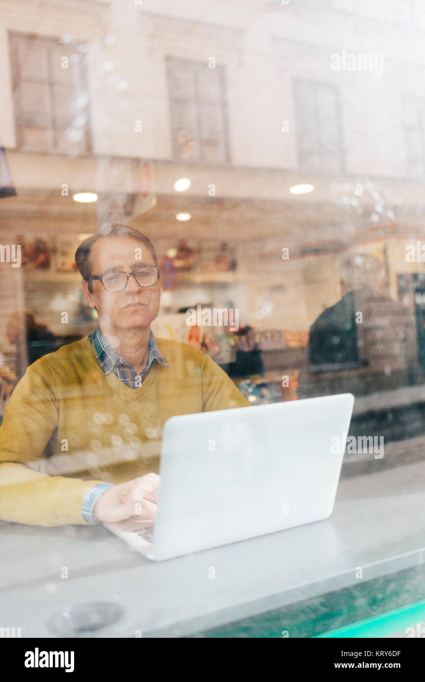 Man using a laptop behind a window Stock Photo