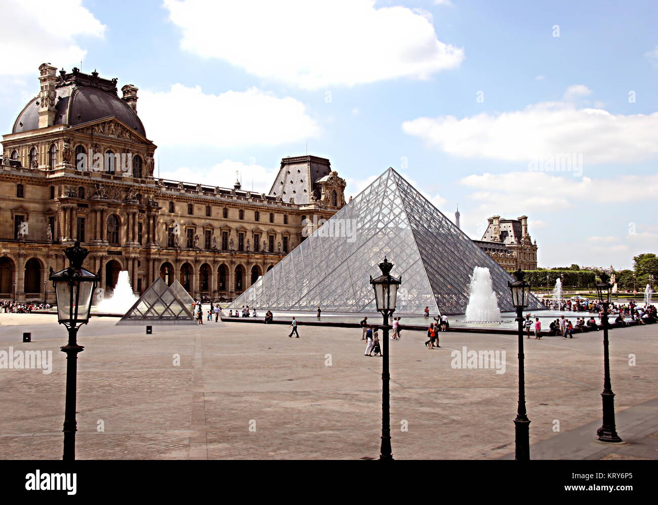 View of the main courtyard of the Louvre Palace with the glass and metal Pyramid (Pyramide du Louvre), and several tourists enjoying the sunny day Stock Photo
