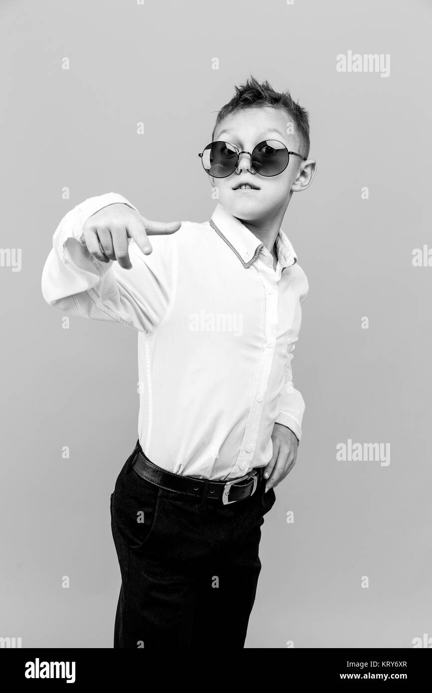 Stylish kid in white shirt and black pants wearing sunglasses posing in studio Stock Photo