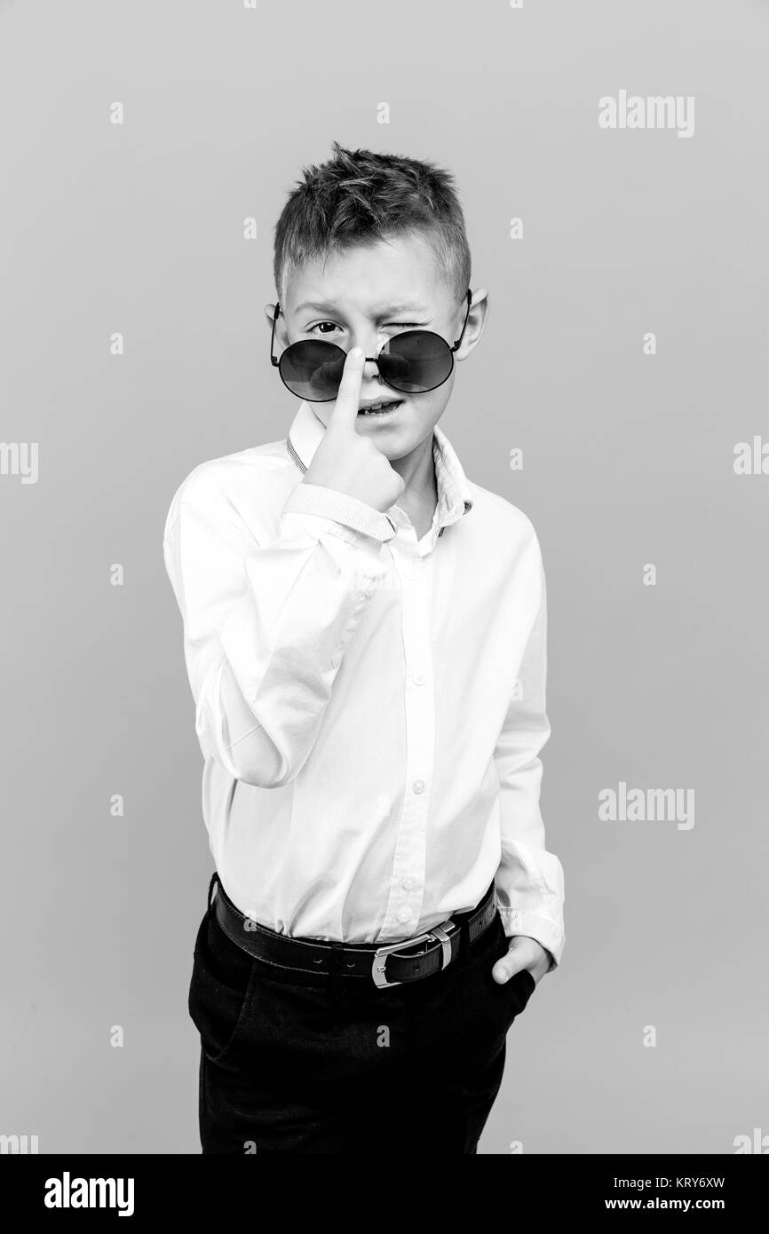 Stylish kid in white shirt and black pants wearing sunglasses posing in studio Stock Photo