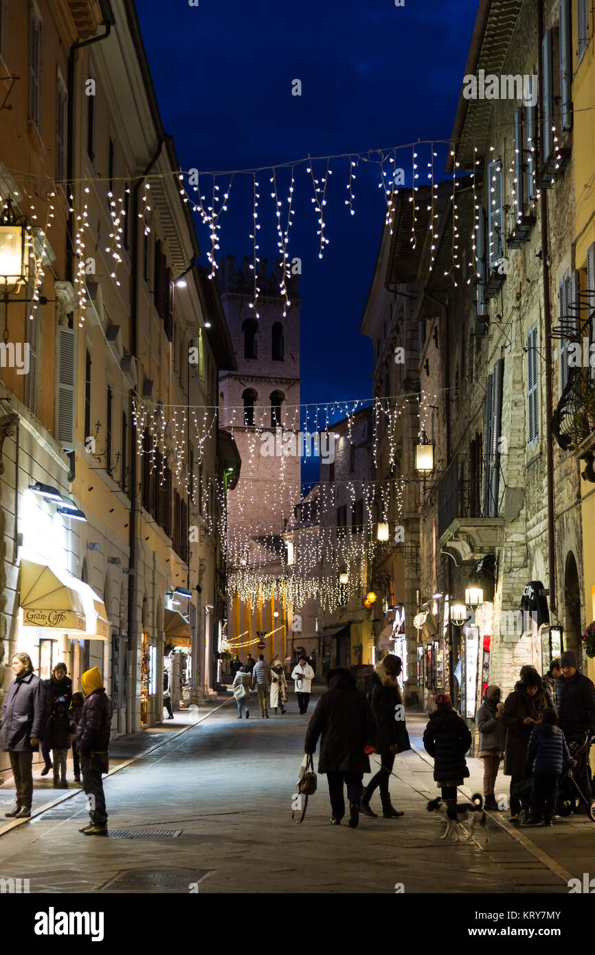 View of main street in Assisi (Umbria) during Christmas time, with people doing shopping, light decorations and the bell tower of Piazza del Comune Stock Photo