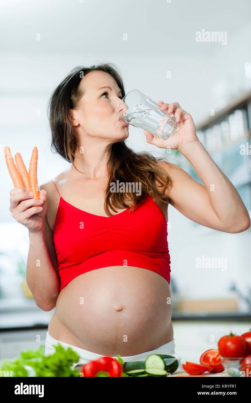 Schwangere Frau mit Gemüse und Wasserglas in der Küche - pregnant woman with vegetables and a glass of water in kitchen Stock Photo
