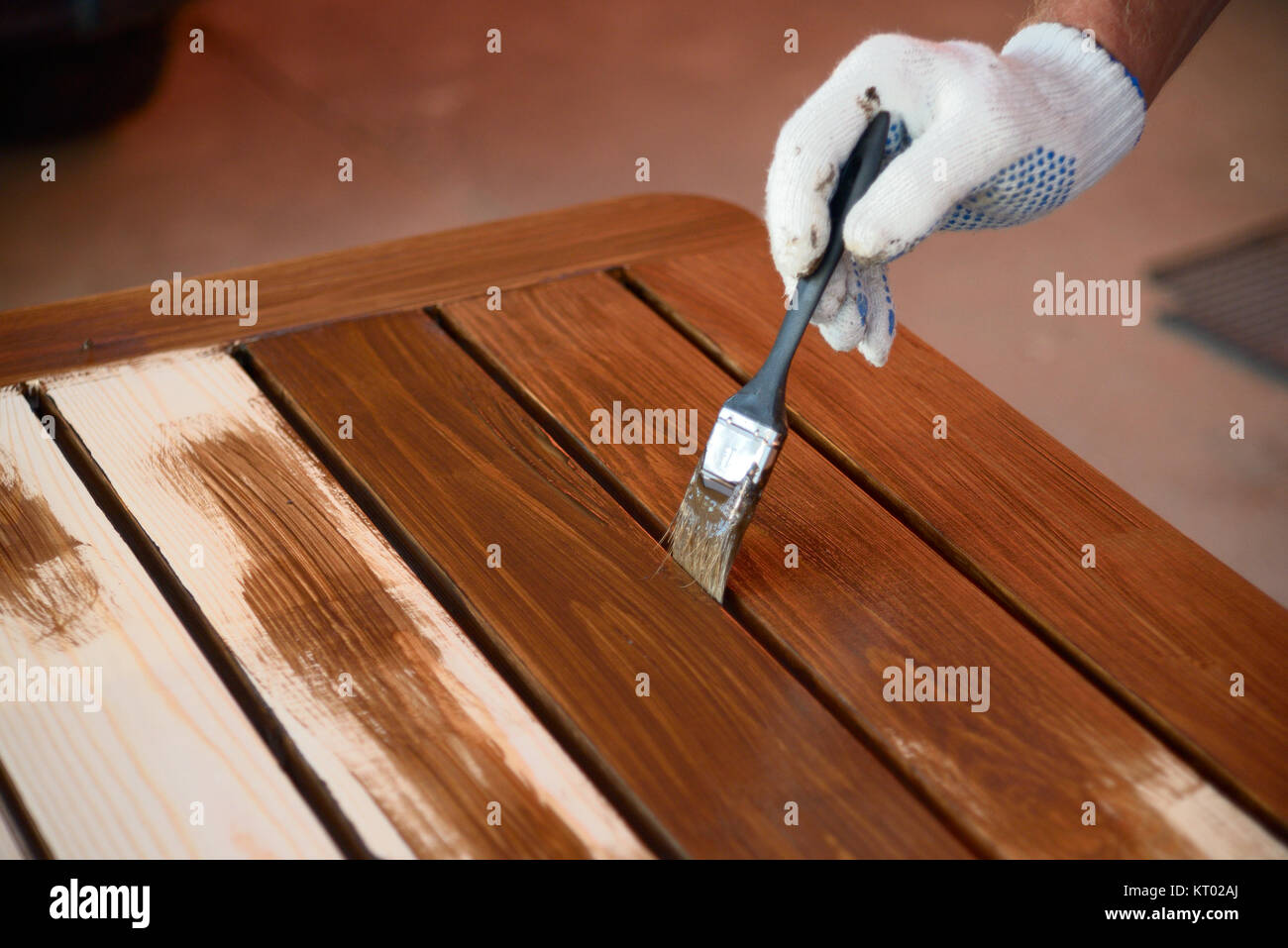 Hand with a brush paints a wooden surface with brown paint, close up Stock Photo