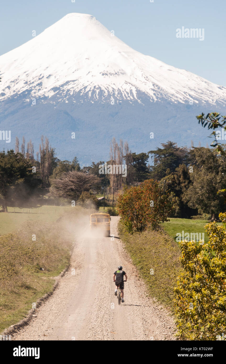 Osorno, Chile - September 28, 2009: A touring cyclist rides behind a traditional yellow school bus on a dirt track in the Los Lagos region of Chilean  Stock Photo