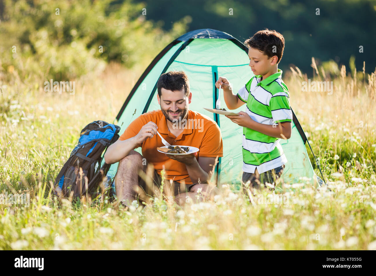 Father and son are camping in nature. They are eating. Stock Photo