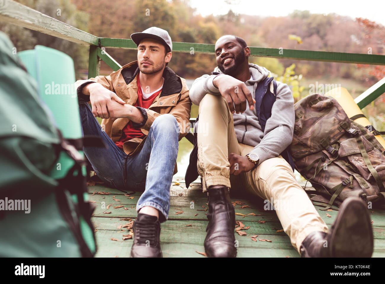 Young men with backpacks sitting on pier Stock Photo Alamy