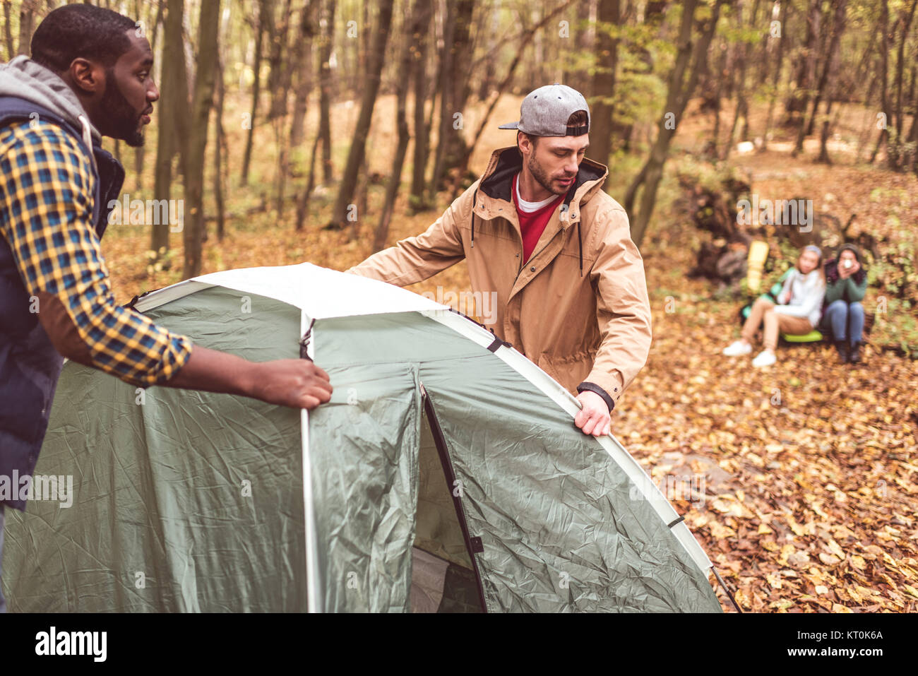 Men pitching tent in autumn forest Stock Photo