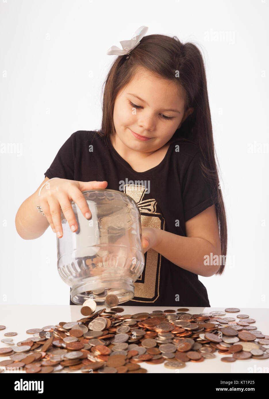 Seven year old girl tipping her savings jar full of coins onto  the desk. Stock Photo