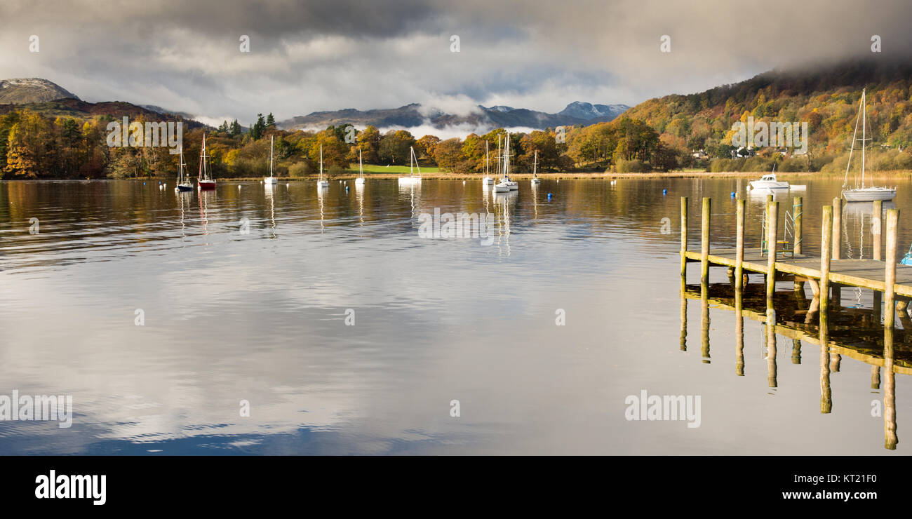 Mist rises from woodland in autumn colour at Ambleside on Windermere lake, under the mountains of Langdale in England's Lake District National Park. Stock Photo