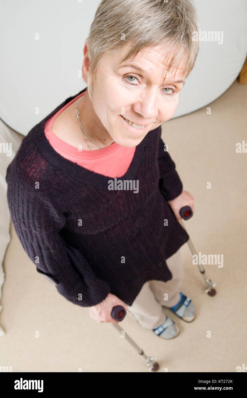 Ganzkörperansicht einer älteren Frau an Krücken im heimischen Wohnzimmer stehend nach einer Hüftoperation. Stock Photo