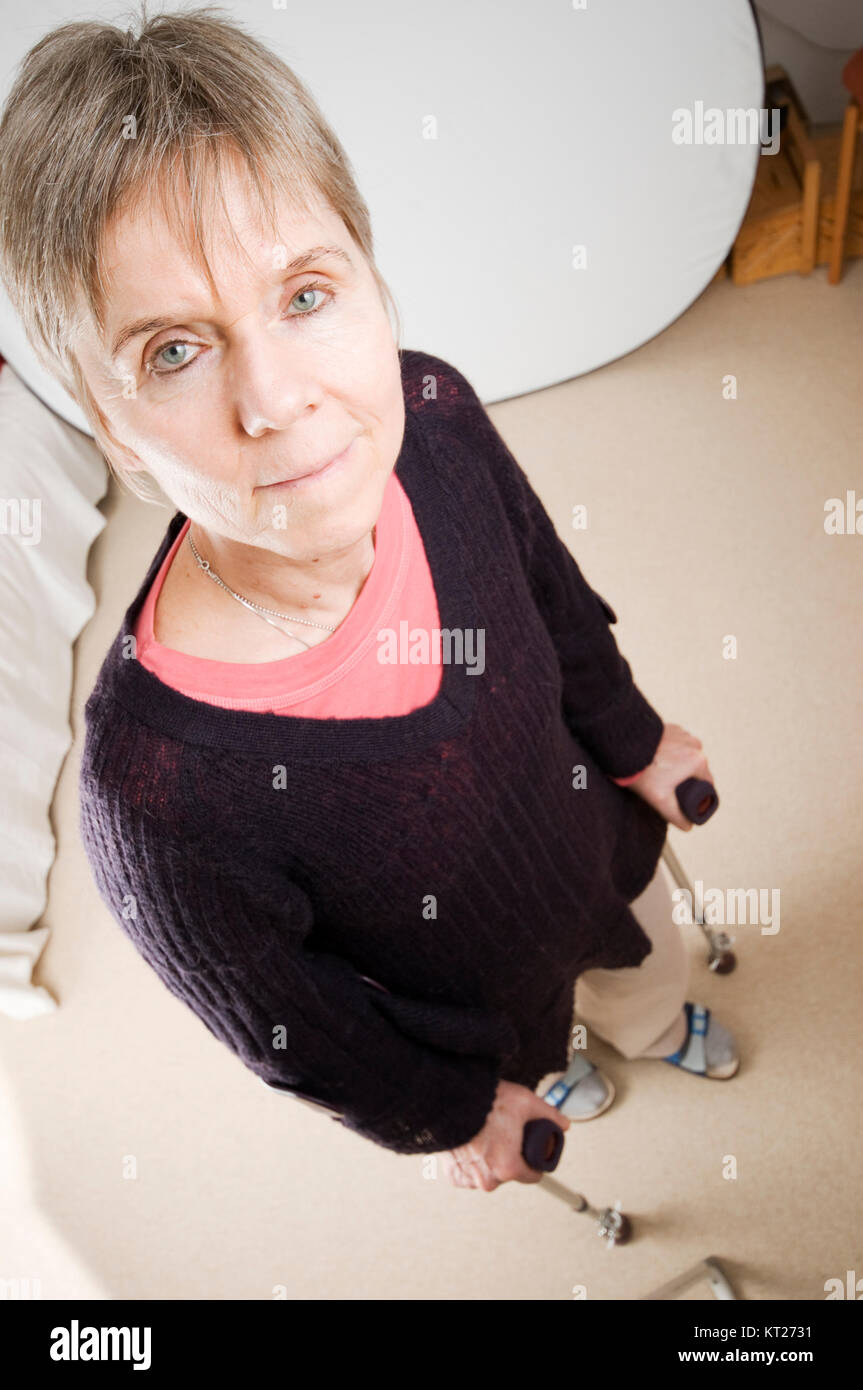 Ganzkörperansicht einer älteren Frau an Krücken im heimischen Wohnzimmer stehend nach einer Hüftoperation. Stock Photo