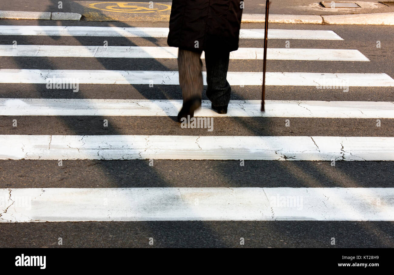 Legs and shadow of a senior person using walking cane while crossing the street Stock Photo