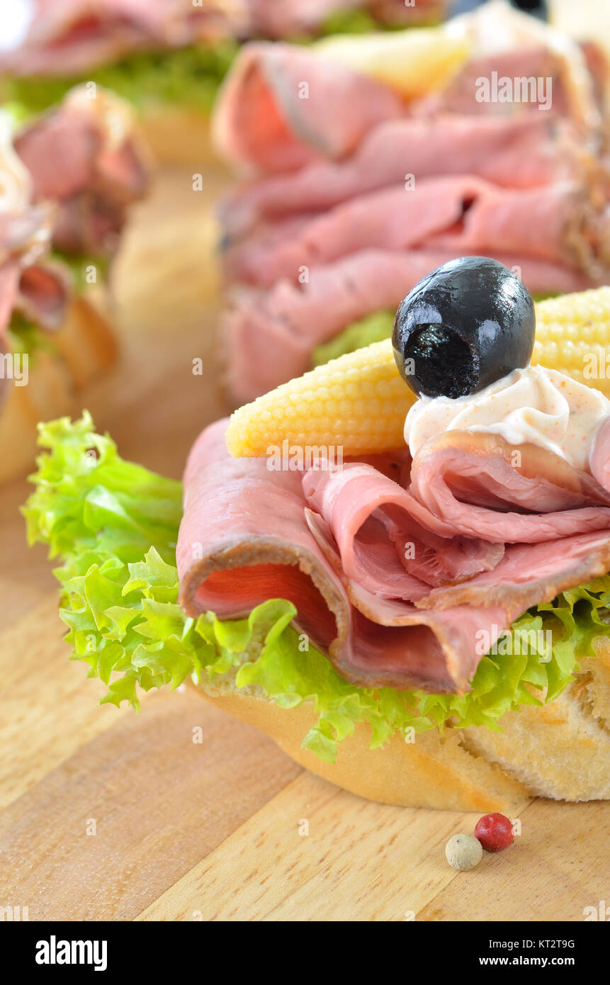 Slices of baguette with roast beef, small corn cobs, paprika cream cheese and black olives Stock Photo