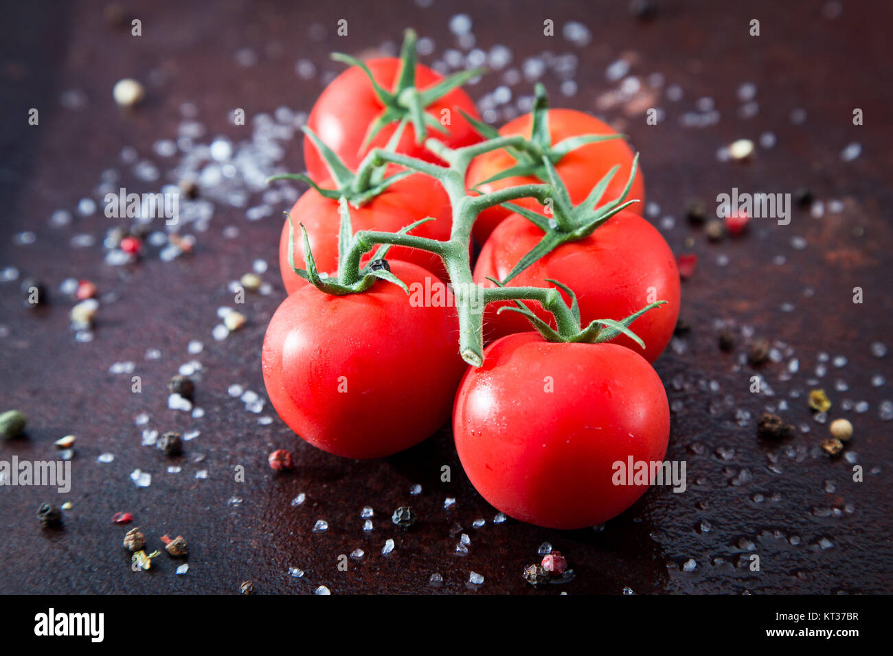 Fresh cherry tomatoes on a black background with spices. Top view with ...