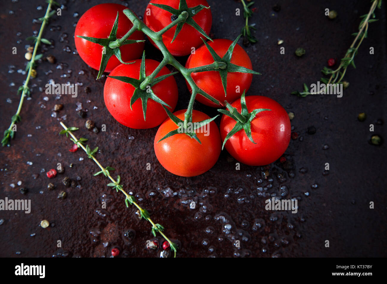 Fresh cherry tomatoes on a black background with spices. Top view with ...