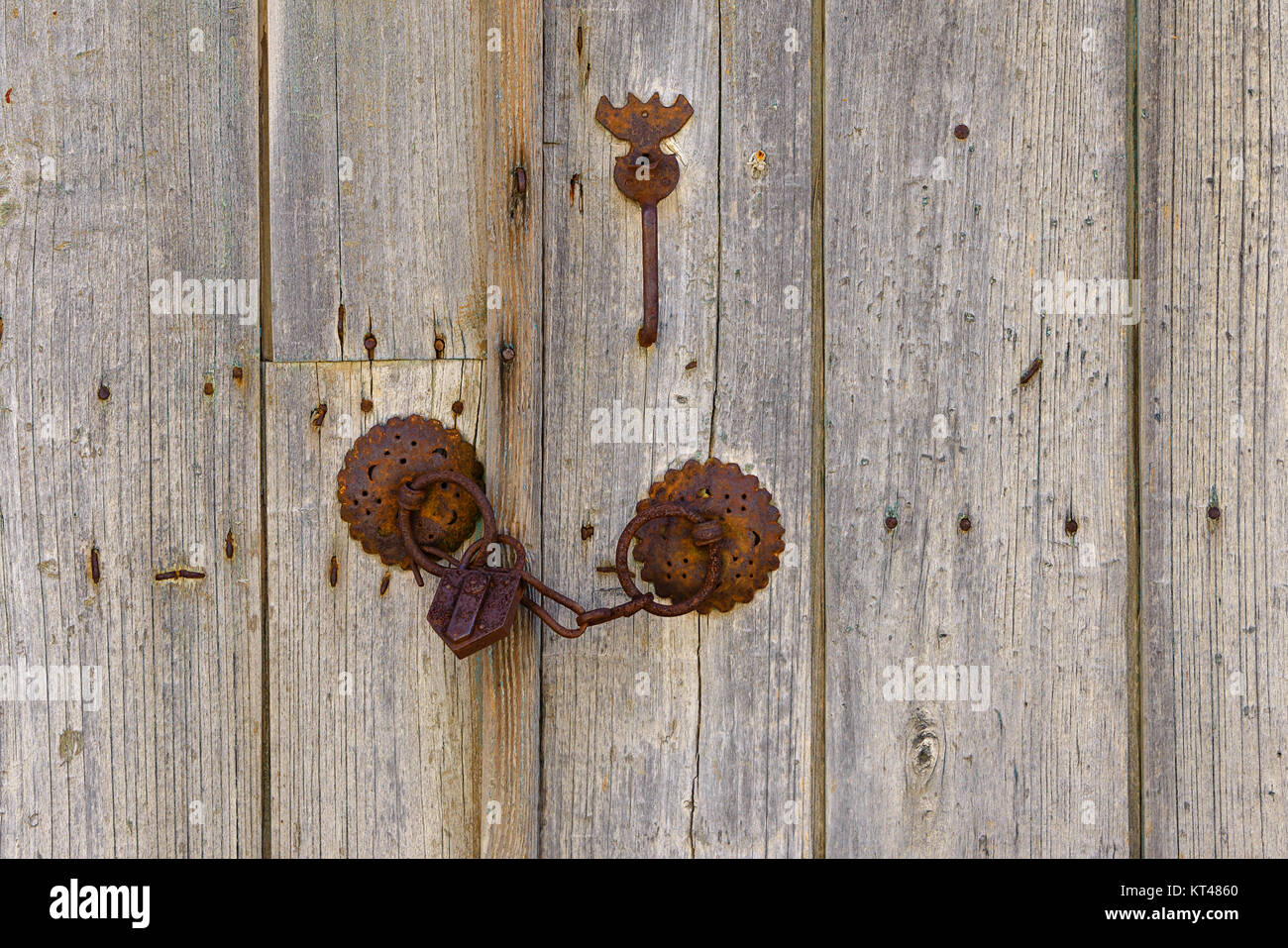 Close up of rusty old iron mountings with chain and padlock on a vintage wooden double door, Greece. Stock Photo
