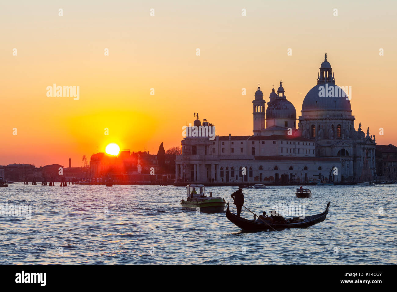 Colourful orange sunset over the Venice lagoon and Basilica di Santa Maria della Salute with boats and a gondola in the foreground, lens flare Stock Photo