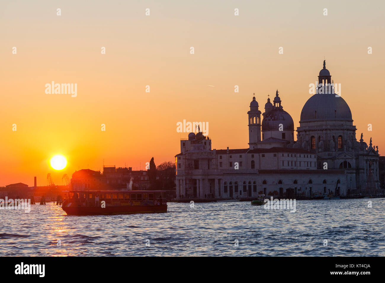 Vivid orange sunset over Basilica di Santa Maria della Salute with a vaporetto passing by on the Grand Canal, Venice, Italy Stock Photo