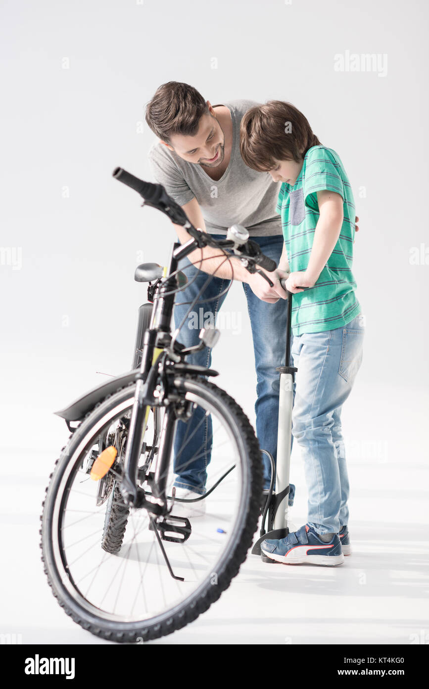 Happy father teaching son to pump up bicycle tire on white Stock Photo