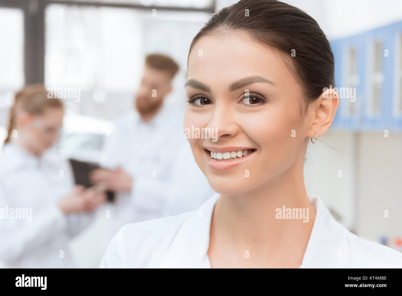 Close-up portrait of young woman in white coat smiling at camera in lab ...